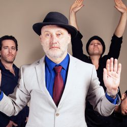 Photo of the band with four people in it, with Jah Wobble at the front holding this hands up.
